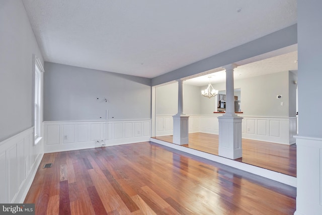 spare room with hardwood / wood-style flooring, an inviting chandelier, a textured ceiling, and ornate columns