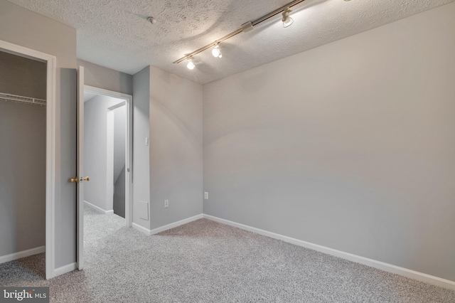 unfurnished bedroom featuring rail lighting, light carpet, a textured ceiling, and a closet