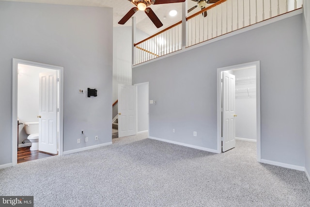 unfurnished living room with carpet flooring, ceiling fan, and a towering ceiling