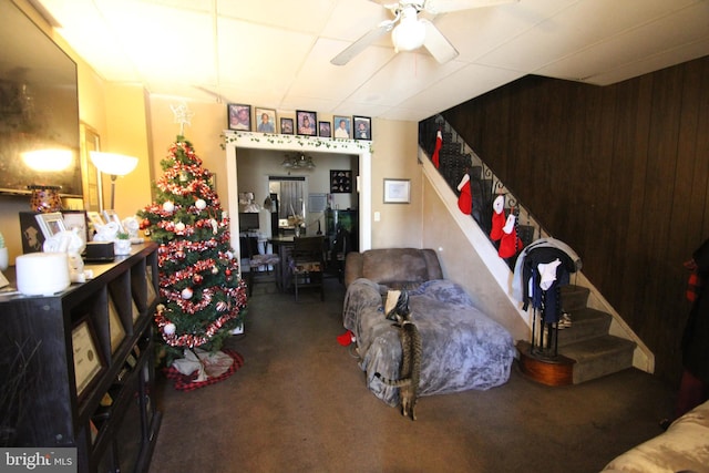 interior space with carpet, a drop ceiling, ceiling fan, and wood walls