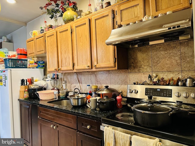 kitchen featuring sink, stainless steel electric range, dark stone countertops, white refrigerator, and decorative backsplash