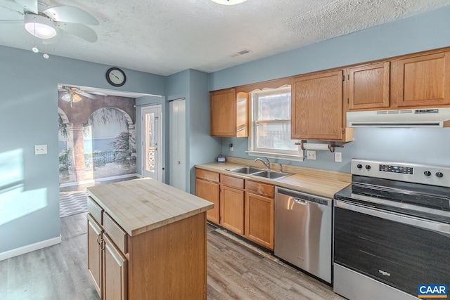 kitchen featuring appliances with stainless steel finishes, sink, light wood-type flooring, a center island, and a textured ceiling