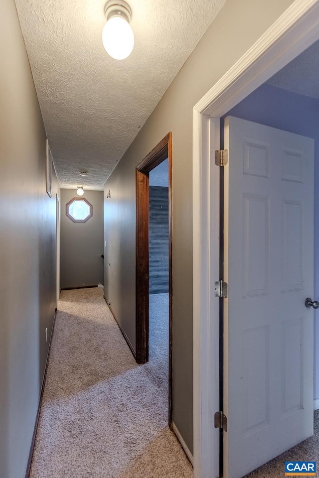 hall with light colored carpet and a textured ceiling