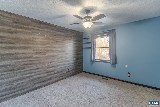 carpeted spare room with ceiling fan, a textured ceiling, and wood walls