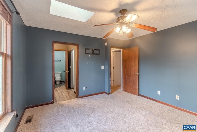 unfurnished bedroom featuring ceiling fan, a skylight, ensuite bathroom, a textured ceiling, and light carpet