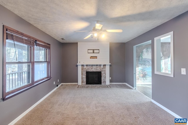 unfurnished living room featuring ceiling fan, carpet flooring, a brick fireplace, and a textured ceiling