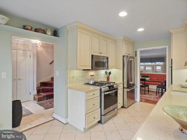 kitchen featuring backsplash, appliances with stainless steel finishes, light tile patterned flooring, and cream cabinetry