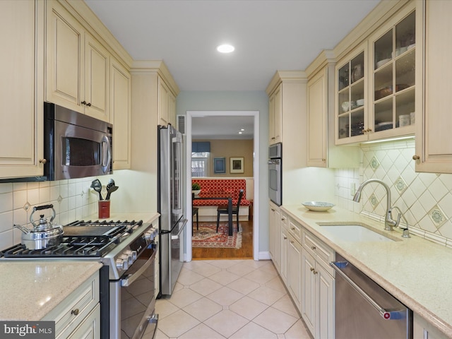 kitchen with appliances with stainless steel finishes, sink, light tile patterned floors, light stone counters, and cream cabinets