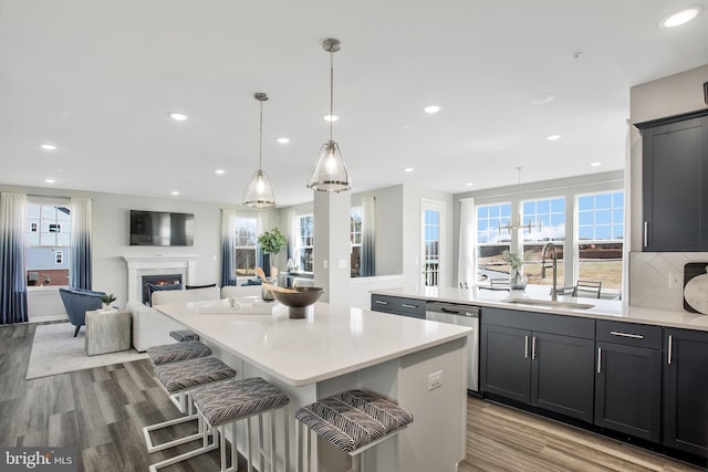 kitchen featuring sink, decorative light fixtures, light hardwood / wood-style flooring, stainless steel dishwasher, and a kitchen island