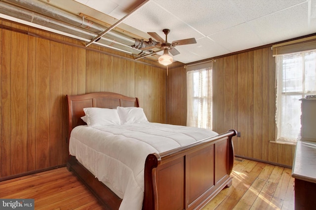 bedroom with ceiling fan, light wood-type flooring, and wooden walls