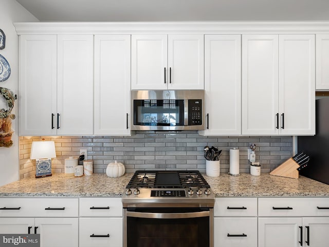 kitchen with stainless steel appliances, white cabinetry, backsplash, and light stone counters