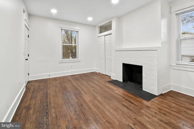 unfurnished living room featuring dark hardwood / wood-style flooring and a brick fireplace