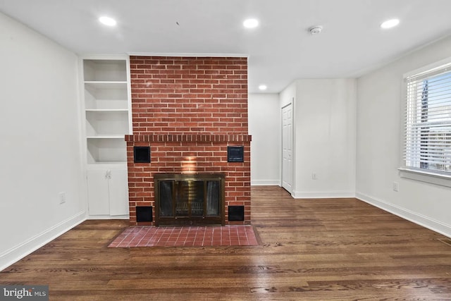 unfurnished living room featuring dark hardwood / wood-style flooring, a brick fireplace, and built in features