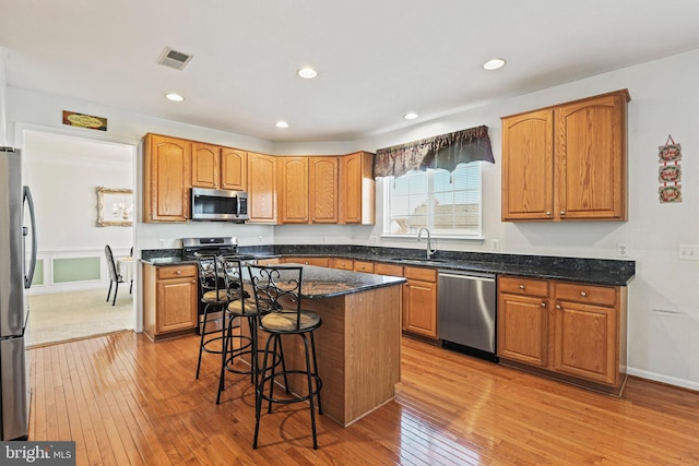 kitchen with visible vents, a kitchen bar, light wood-style flooring, stainless steel appliances, and a sink