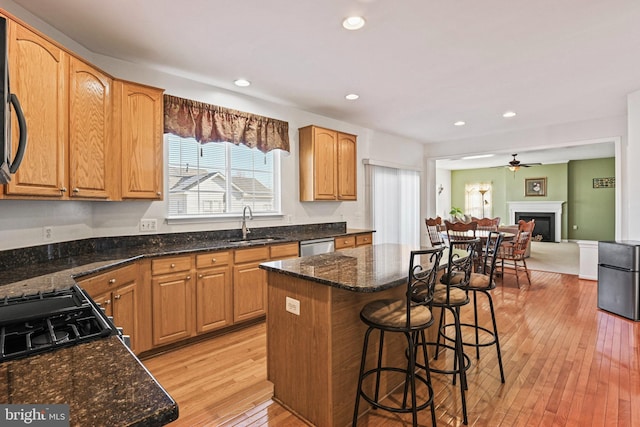 kitchen with a sink, a kitchen island, a breakfast bar area, a fireplace, and light wood finished floors