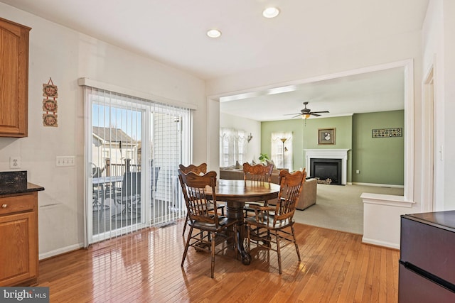 dining area with a ceiling fan, baseboards, recessed lighting, light wood-style floors, and a glass covered fireplace