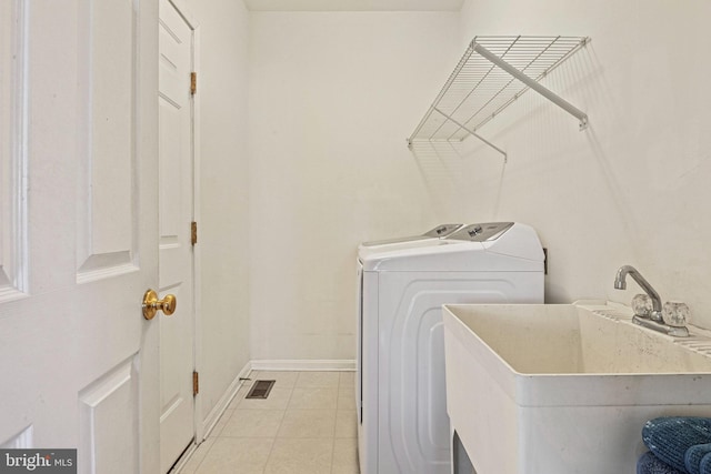 washroom with baseboards, washing machine and dryer, light tile patterned floors, laundry area, and a sink