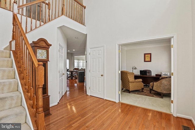 entrance foyer with light wood-type flooring, visible vents, baseboards, a towering ceiling, and stairs