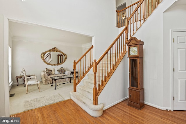 stairway with a towering ceiling, baseboards, wood-type flooring, and ornamental molding