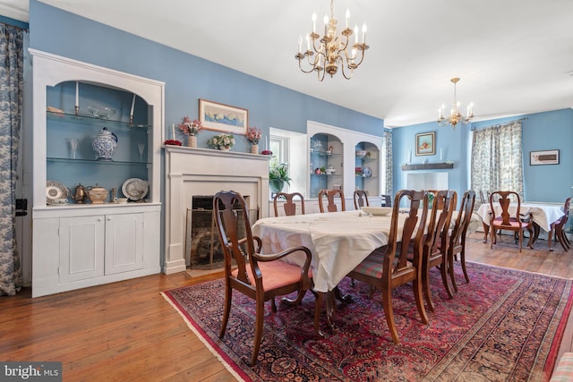 dining space with hardwood / wood-style flooring, built in features, and an inviting chandelier