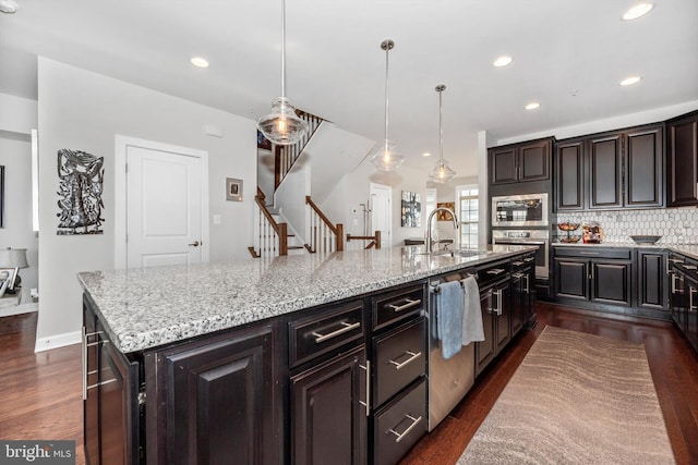 kitchen with sink, hanging light fixtures, dark hardwood / wood-style floors, decorative backsplash, and a large island with sink