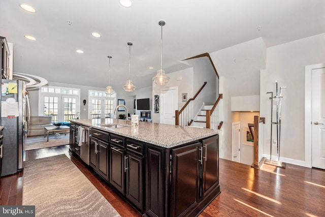 kitchen with pendant lighting, sink, stainless steel appliances, light stone countertops, and a center island with sink