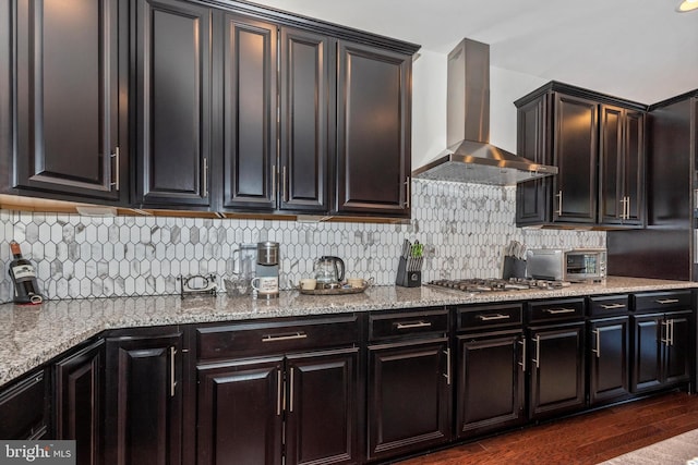 kitchen featuring dark hardwood / wood-style floors, backsplash, stainless steel gas cooktop, light stone countertops, and wall chimney exhaust hood