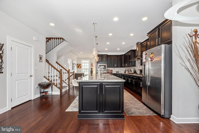 kitchen featuring light stone counters, an island with sink, decorative backsplash, stainless steel fridge with ice dispenser, and decorative light fixtures