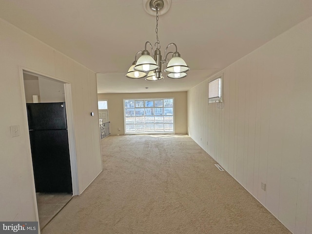 unfurnished dining area with light carpet, a notable chandelier, and wood walls