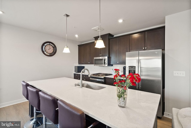 kitchen featuring pendant lighting, tasteful backsplash, an island with sink, sink, and stainless steel appliances