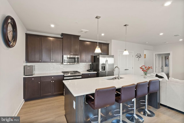 kitchen featuring sink, appliances with stainless steel finishes, backsplash, a kitchen bar, and decorative light fixtures