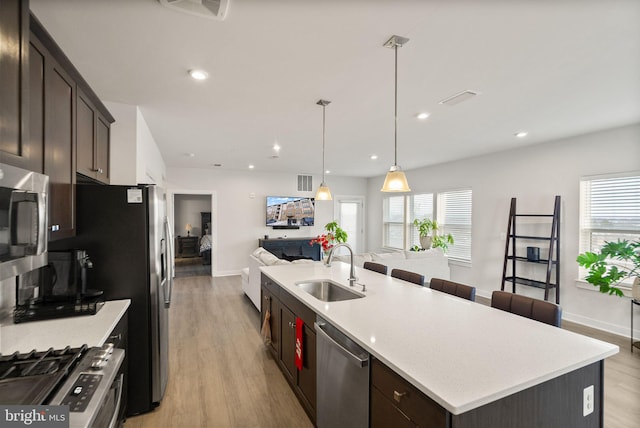 kitchen featuring sink, hanging light fixtures, a center island with sink, light wood-type flooring, and appliances with stainless steel finishes