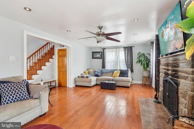 living room with ceiling fan, stairway, wood finished floors, a stone fireplace, and recessed lighting