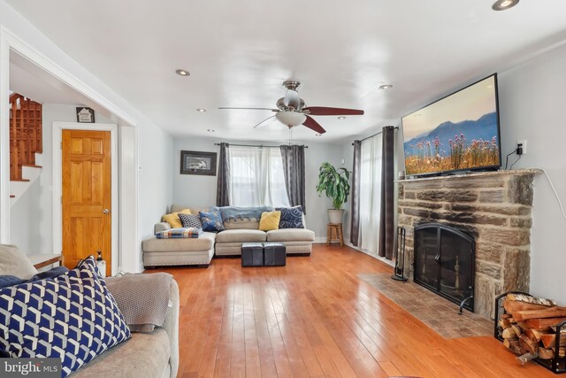 living area with a ceiling fan, hardwood / wood-style flooring, stairway, a stone fireplace, and recessed lighting