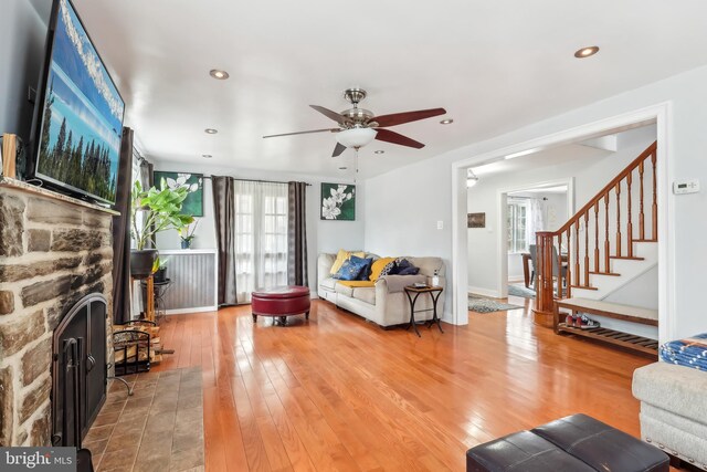 living room with hardwood / wood-style flooring, ceiling fan, stairway, and a stone fireplace