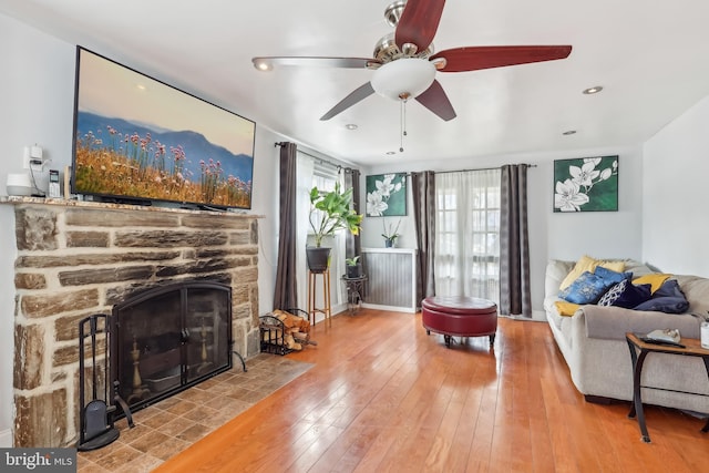 living room featuring recessed lighting, wood-type flooring, a stone fireplace, and baseboards