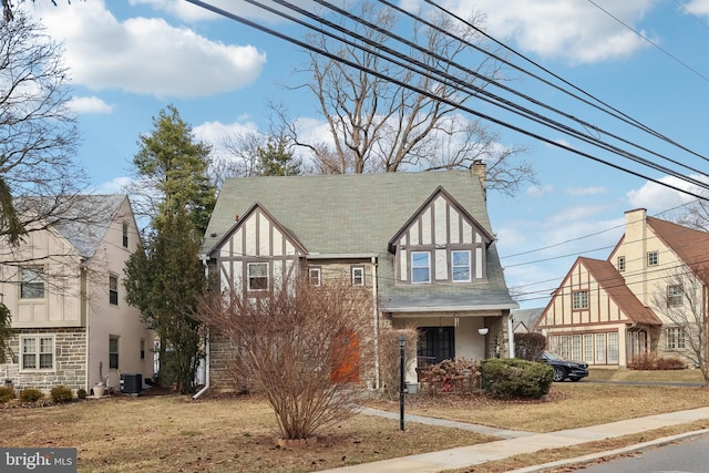 tudor house with a chimney, stucco siding, central air condition unit, stone siding, and a front lawn