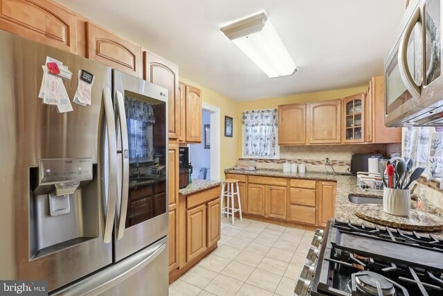 kitchen featuring glass insert cabinets, appliances with stainless steel finishes, light stone counters, backsplash, and light tile patterned flooring