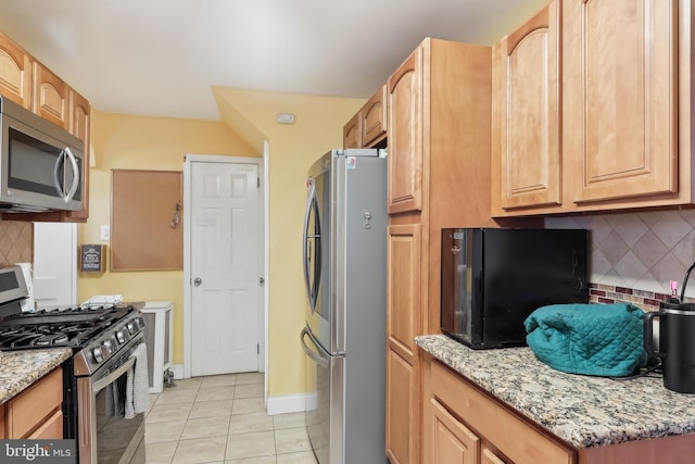 kitchen with light tile patterned floors, baseboards, appliances with stainless steel finishes, light stone countertops, and tasteful backsplash