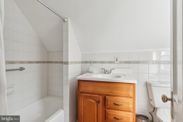 full bathroom featuring tile walls, toilet, lofted ceiling, vanity, and a bath