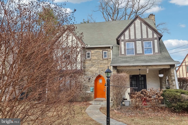 tudor-style house featuring stone siding, roof with shingles, a chimney, and stucco siding