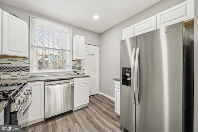 kitchen featuring appliances with stainless steel finishes, white cabinetry, backsplash, light hardwood / wood-style floors, and dark stone counters