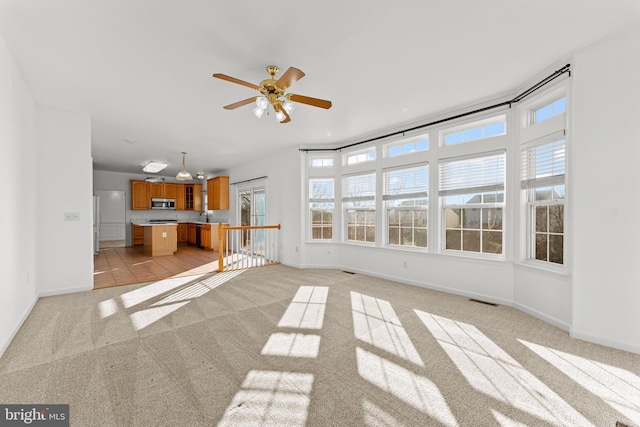 unfurnished living room featuring sink, light colored carpet, and ceiling fan