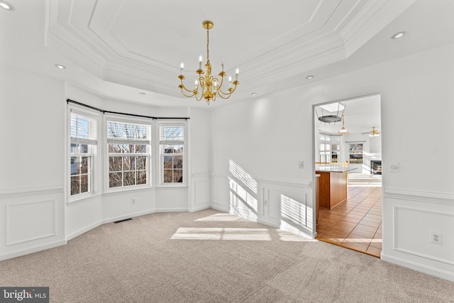 empty room with ornamental molding, a raised ceiling, ceiling fan with notable chandelier, and light carpet