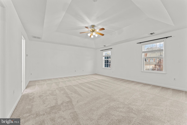 unfurnished room with ceiling fan, a tray ceiling, and light carpet