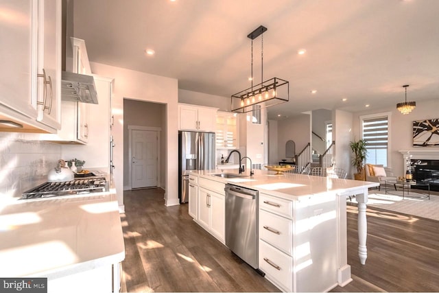 kitchen featuring appliances with stainless steel finishes, an island with sink, sink, white cabinets, and hanging light fixtures