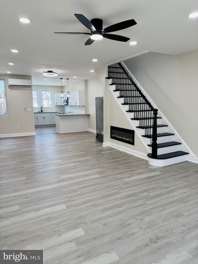 unfurnished living room with sink, light hardwood / wood-style flooring, a wall unit AC, and ceiling fan