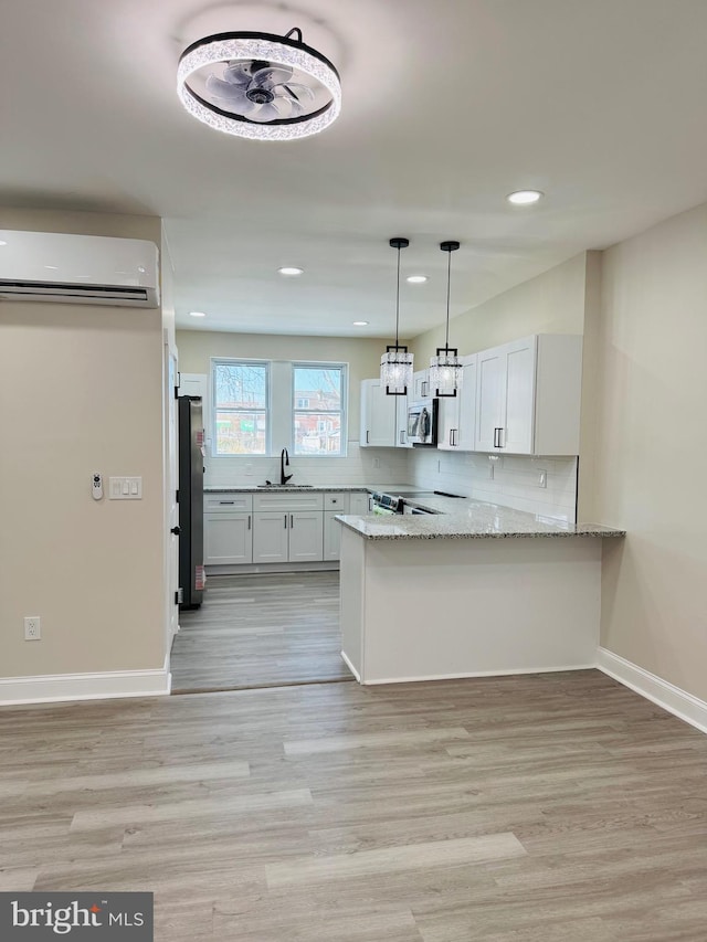 kitchen featuring white cabinetry, stainless steel appliances, kitchen peninsula, and a wall unit AC