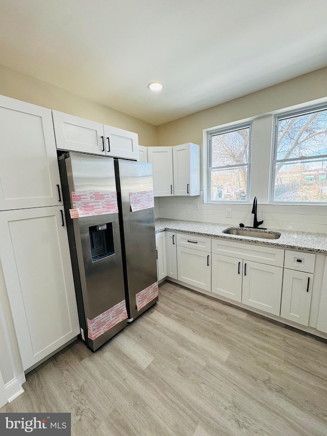 kitchen featuring white cabinets, light stone countertops, sink, and stainless steel fridge