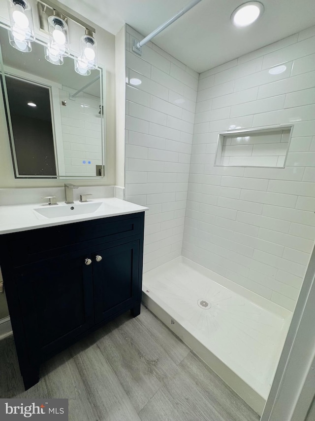 bathroom featuring wood-type flooring, tiled shower, and vanity